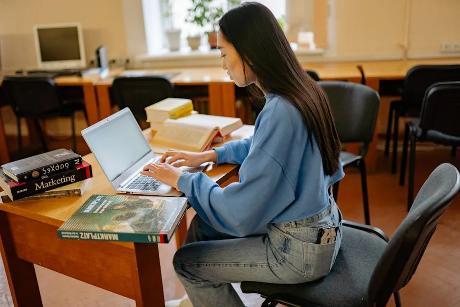 Focused woman typing on laptop, surrounded by books in a cozy study spot.